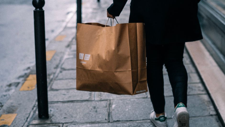A person walking on the street carrying a brown paper shopping bag, symbolizing urban shopping.